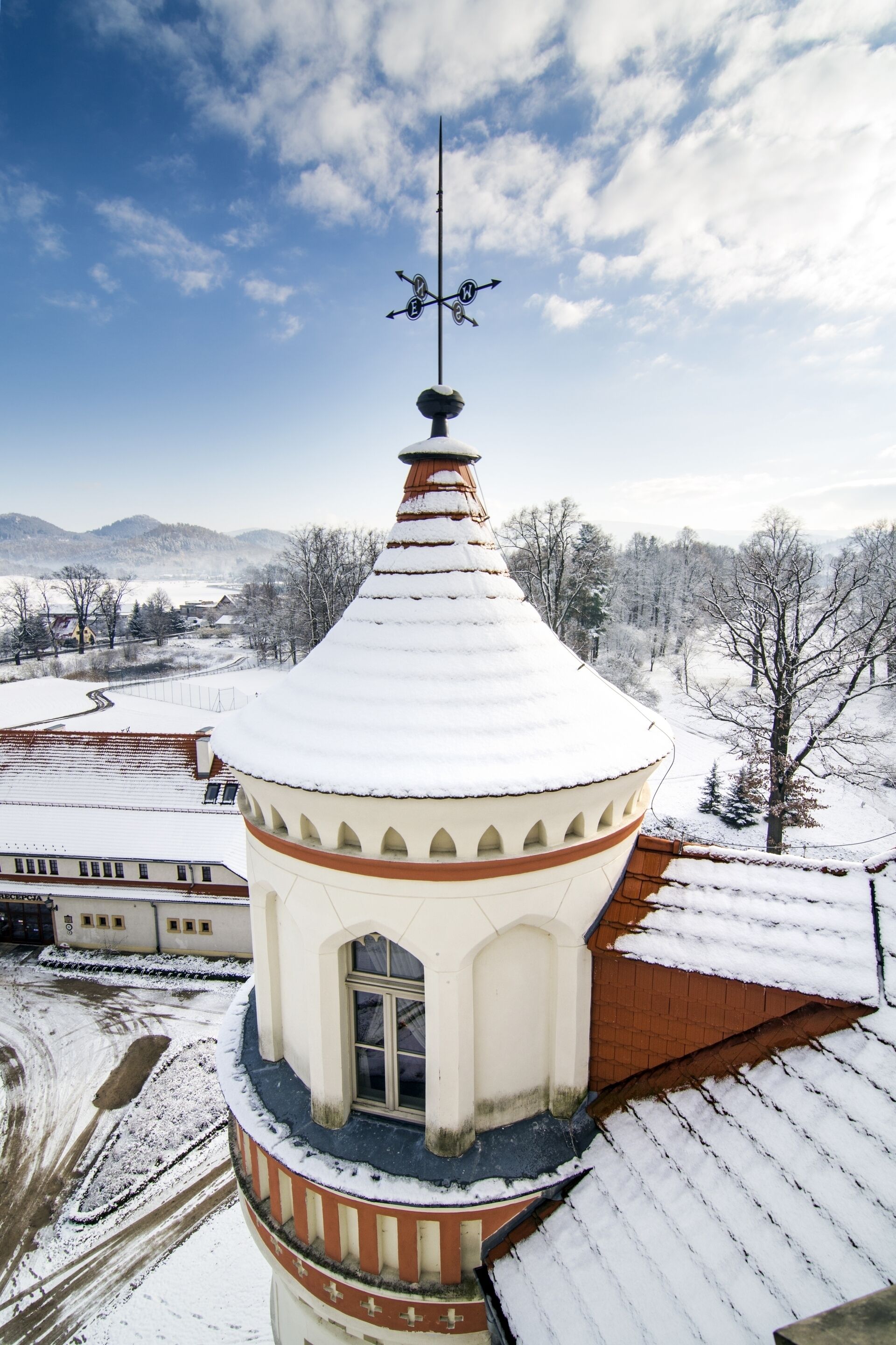 A snow-covered tower with a weather vane, surrounded by a snowy landscape and buildings.