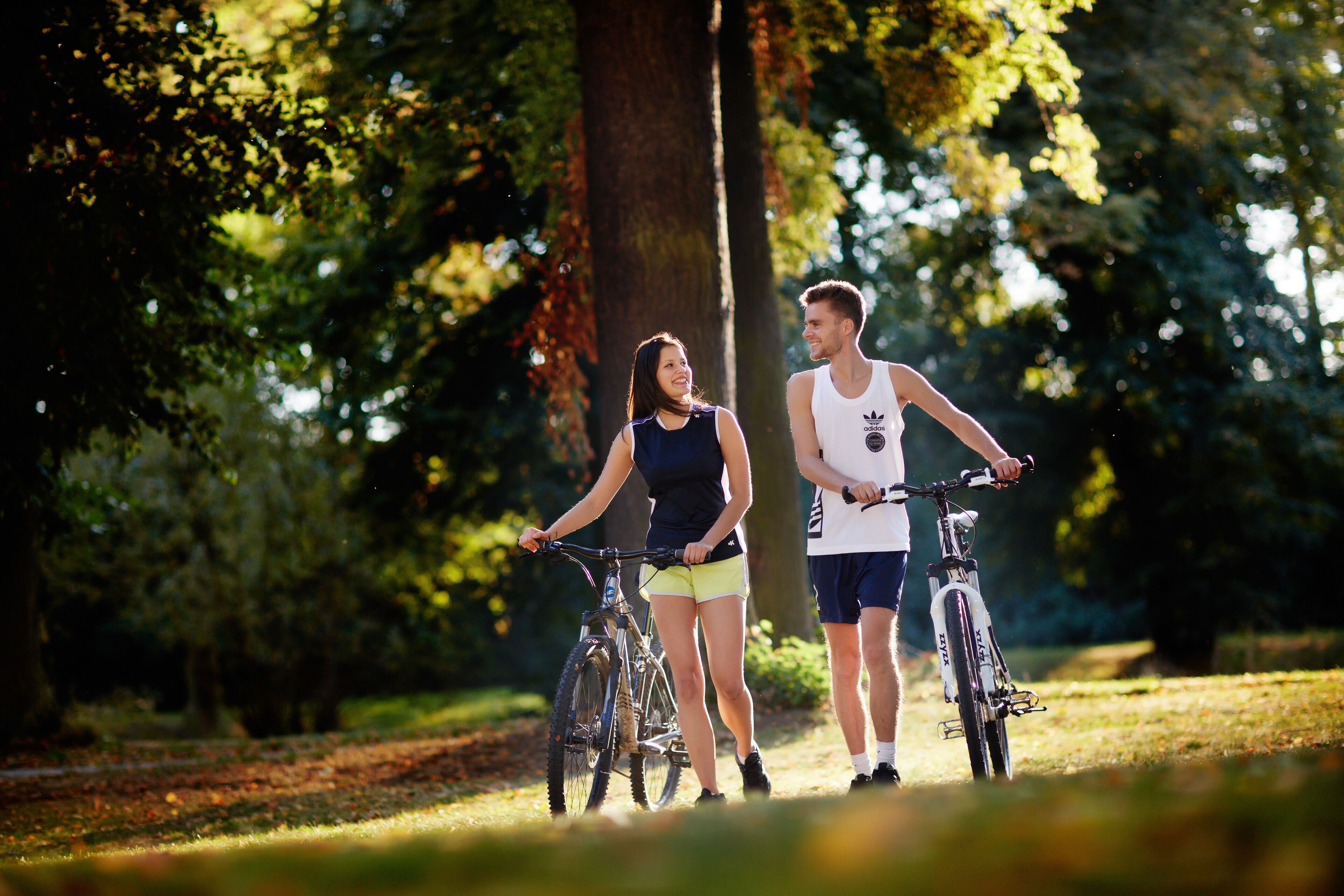 Dos personas en bicicleta en un parque con árboles y césped.