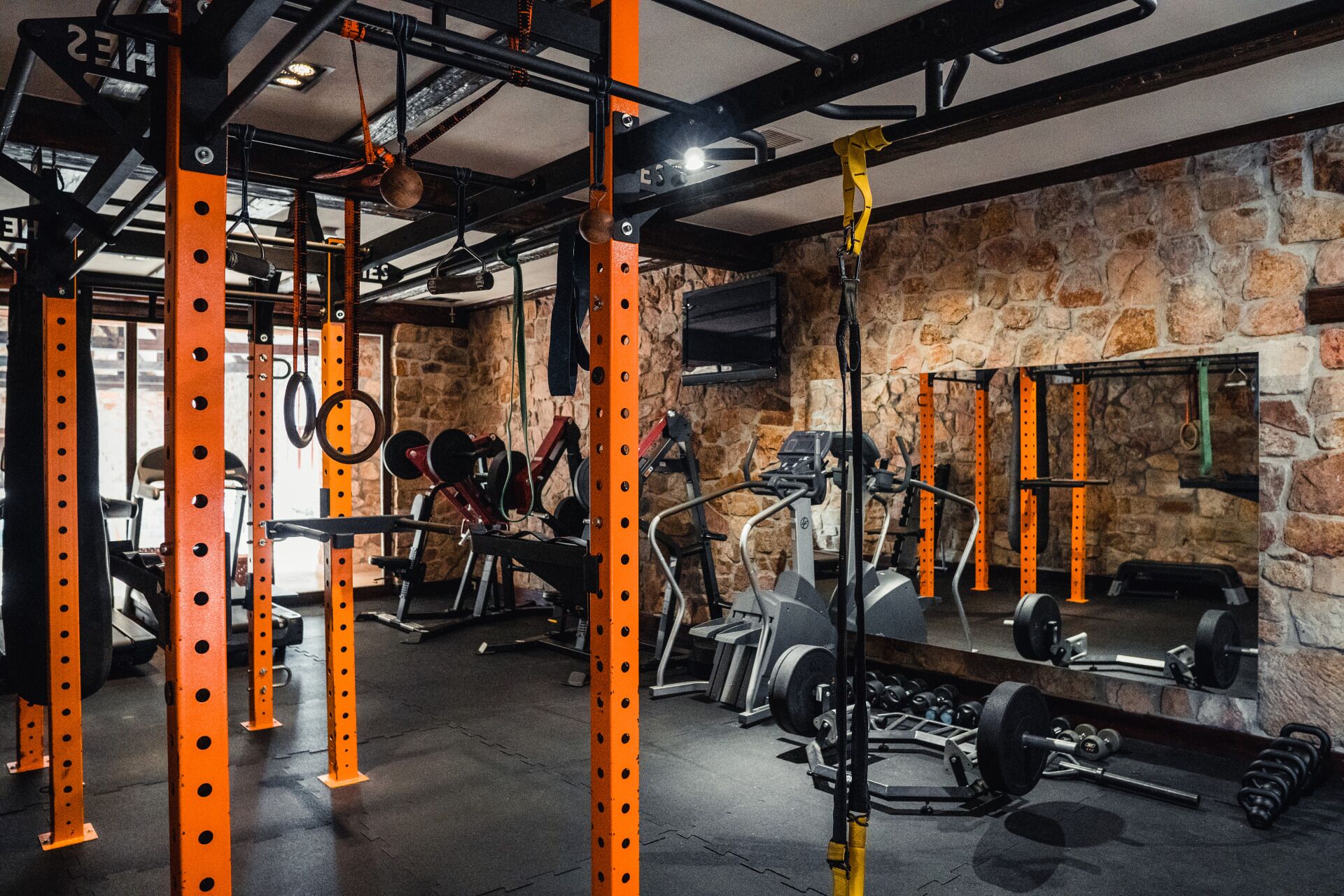 A gym with orange metal frames, weightlifting equipment, and a stone wall.
