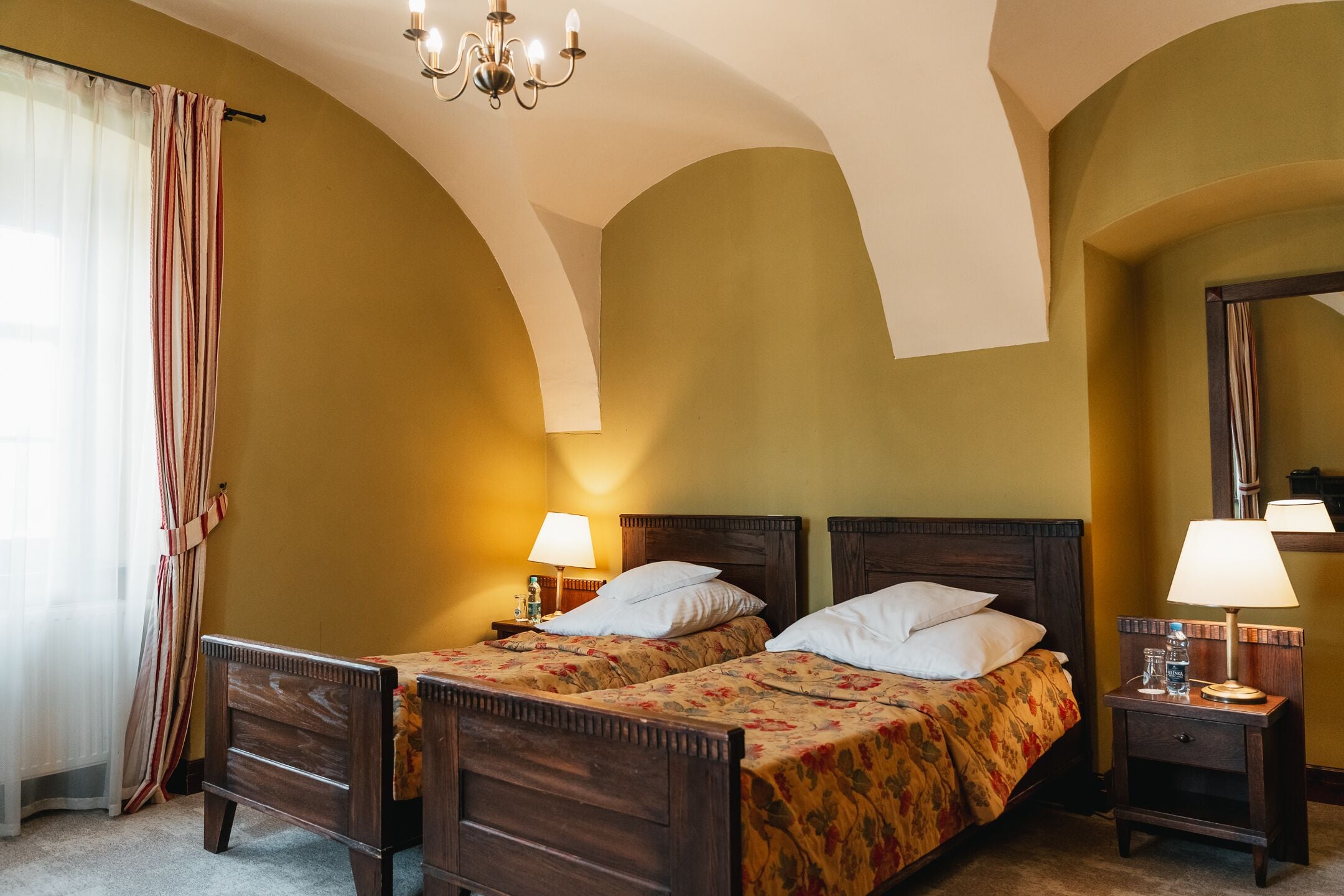 Una habitación de hotel con dos camas de madera, un candelabro y un espejo en la pared.