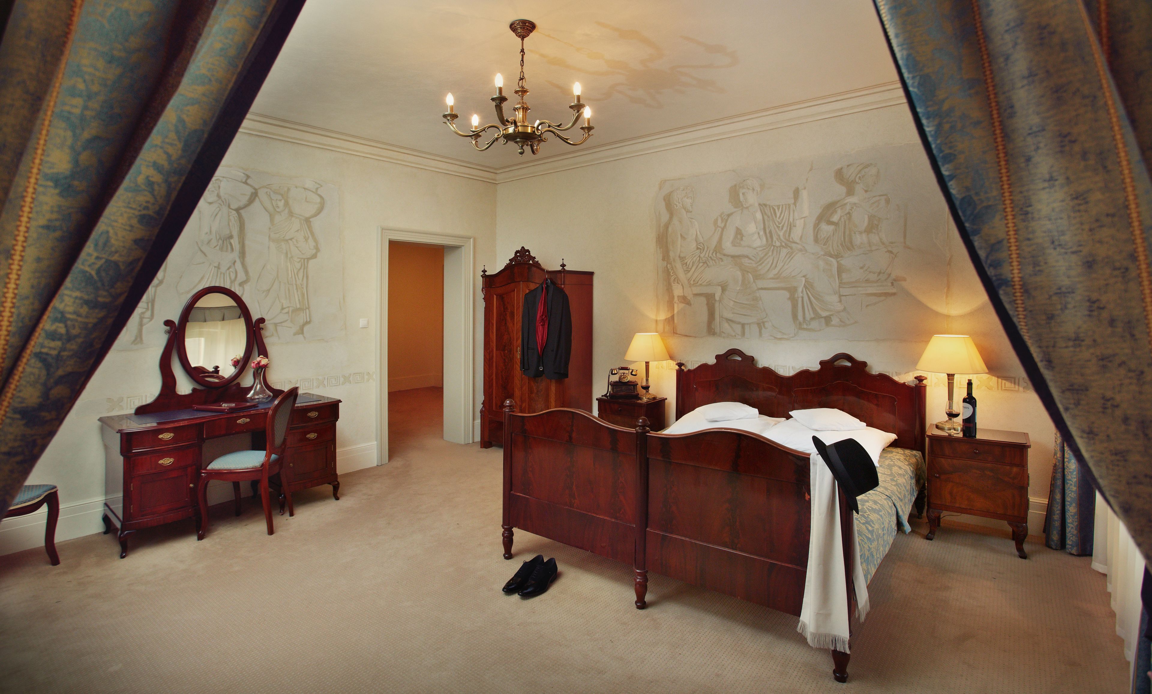 A bedroom with a large bed, a dresser, a vanity with a mirror, and a chandelier.