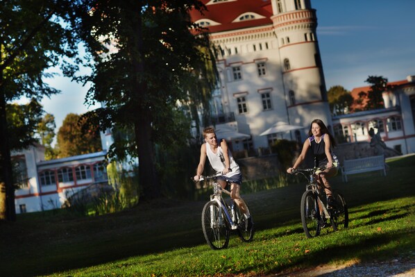 Two people riding bicycles on a grassy path with a historic building in the background. - Palac Wojanow (Myslakowice)