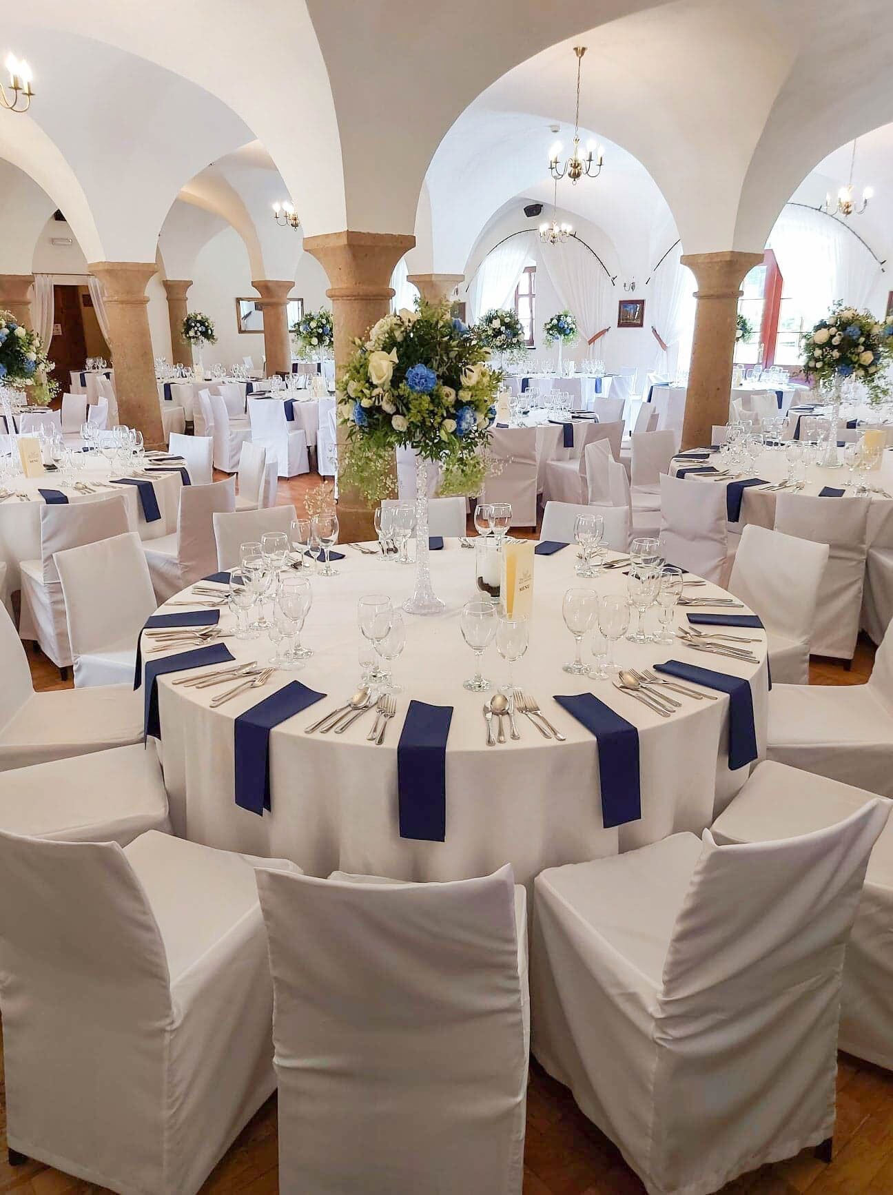 A banquet hall with round tables, white chairs, and blue napkins.