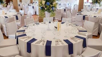A banquet hall with round tables, white chairs, and blue napkins.