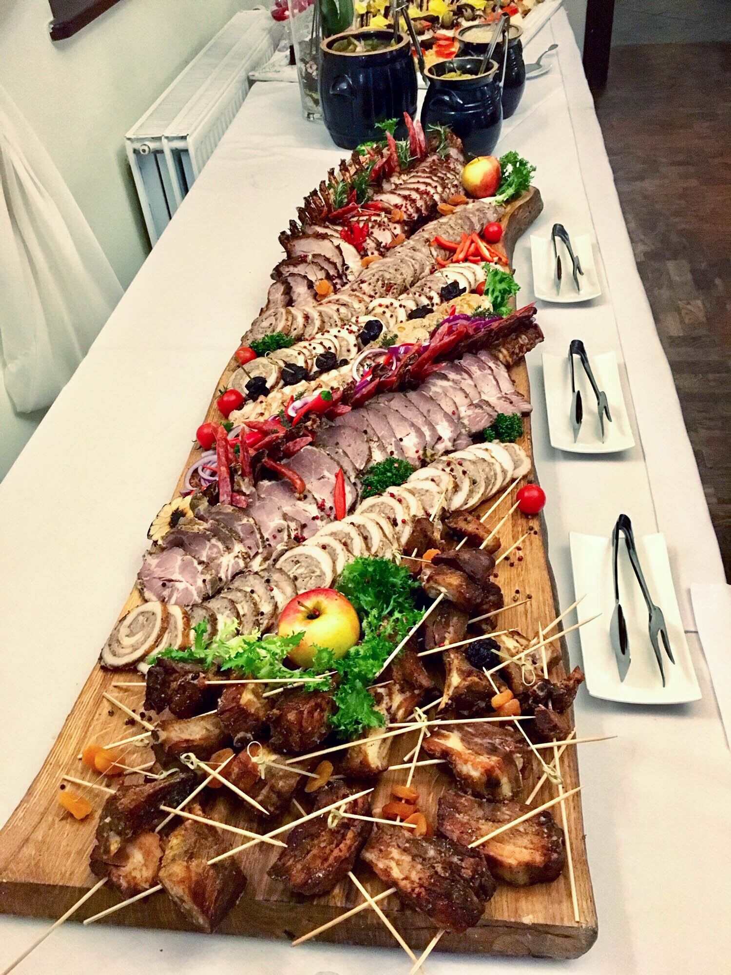 A long table with various meats and vegetables, including skewers and a large apple.