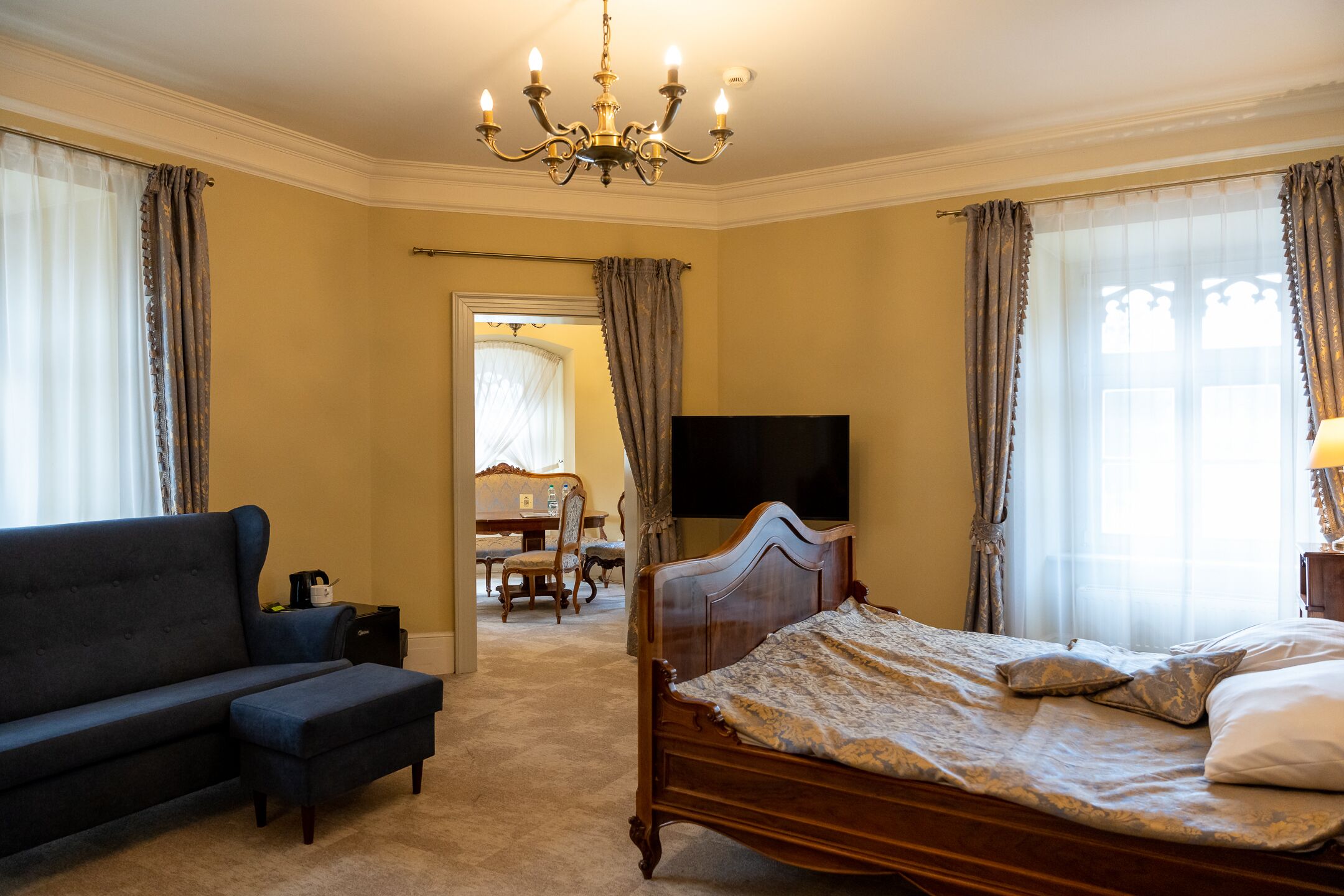 Een slaapkamer met een bed, een bank, een televisie en een kroonluchter.