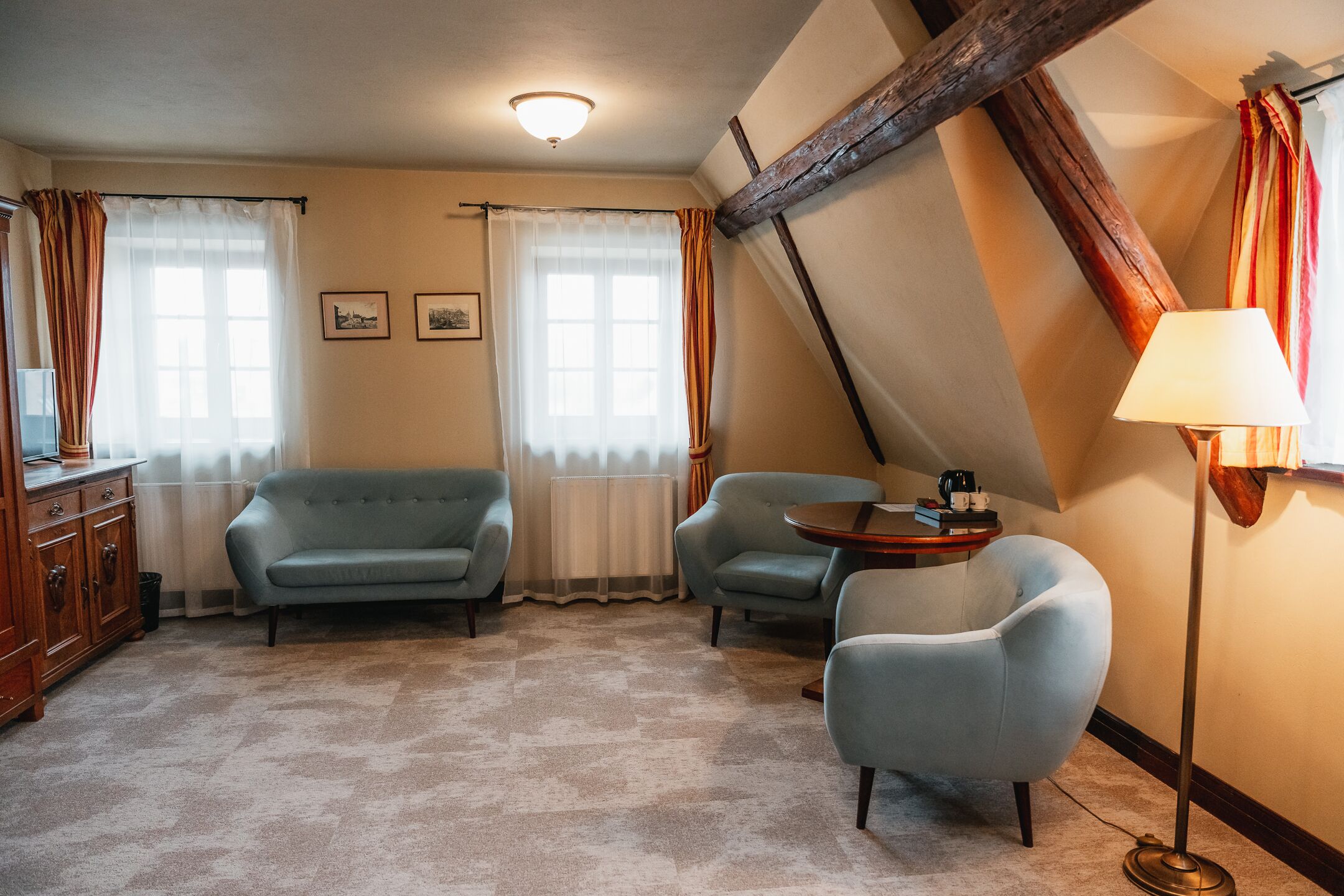 Ein Zimmer mit einer Couch, zwei Sesseln, einem kleinen Tisch und einer Lampe.