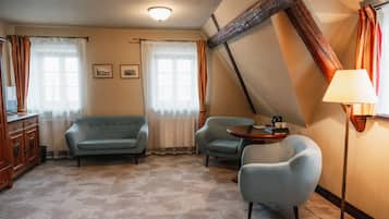 Ein Zimmer mit einer Couch, zwei Sesseln, einem kleinen Tisch und einer Lampe.