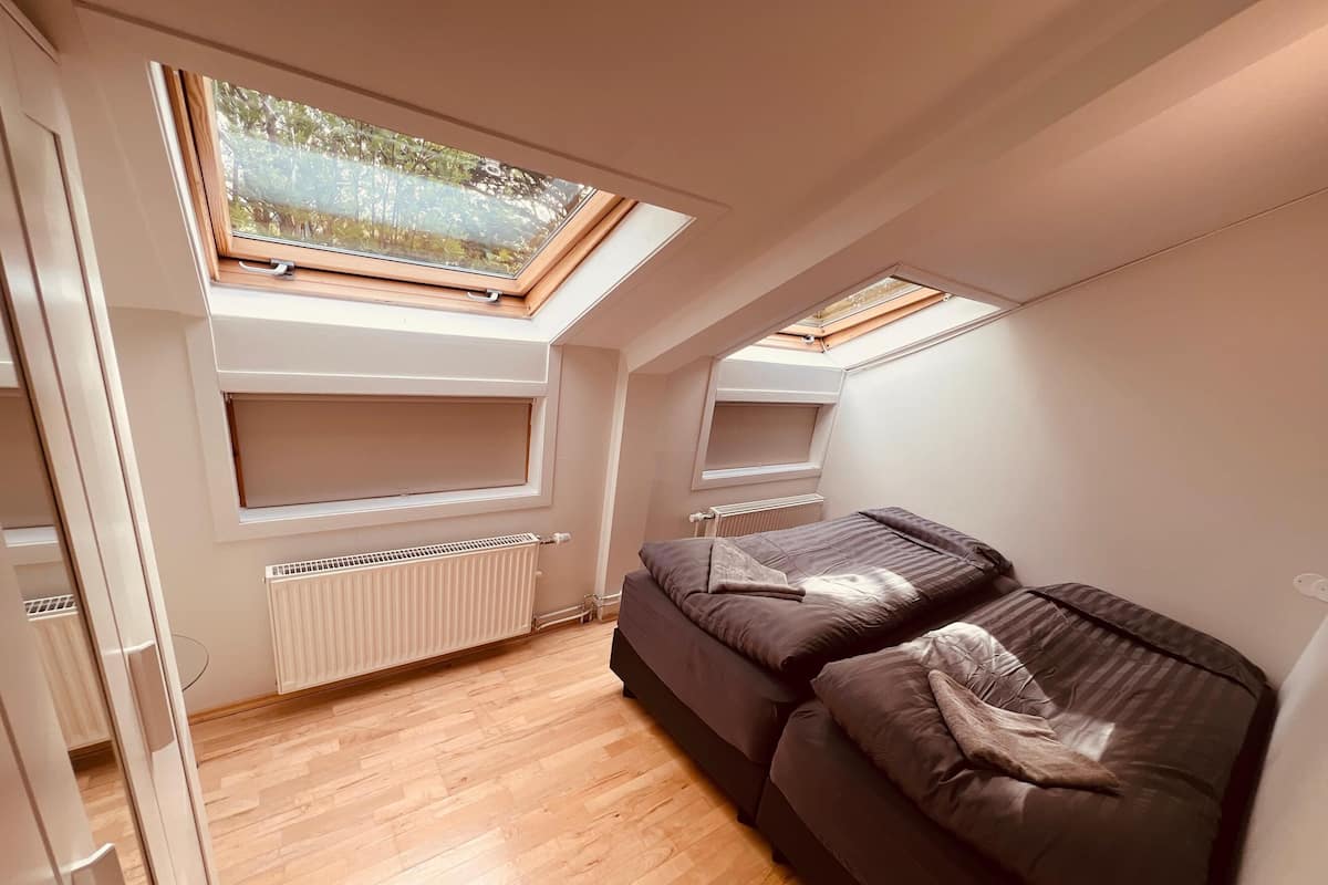 A compact room with a sloped ceiling, skylights, a radiator, and a dark-colored sofa.