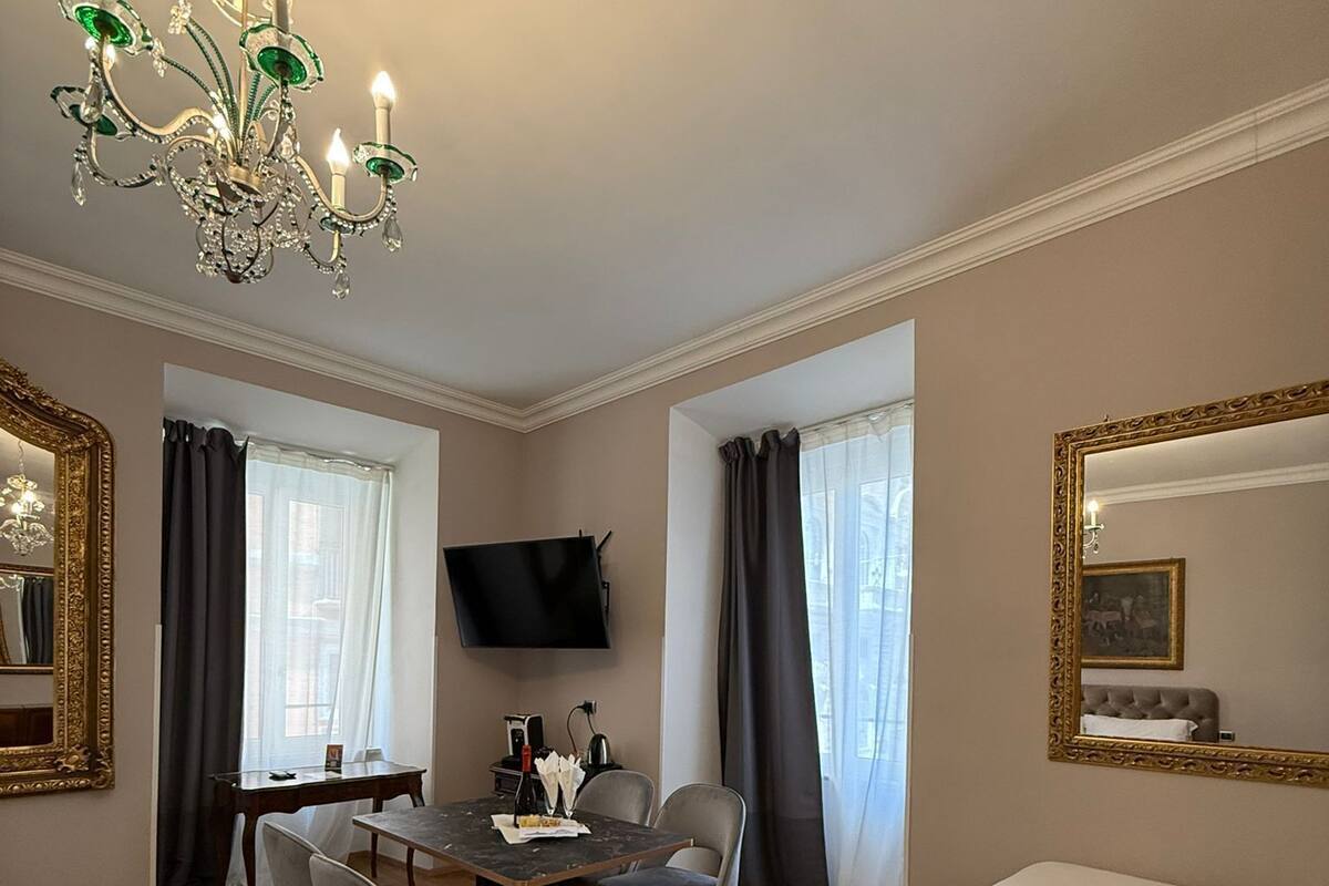 A room with a dining table, chairs, a sofa, a TV, and a chandelier.
