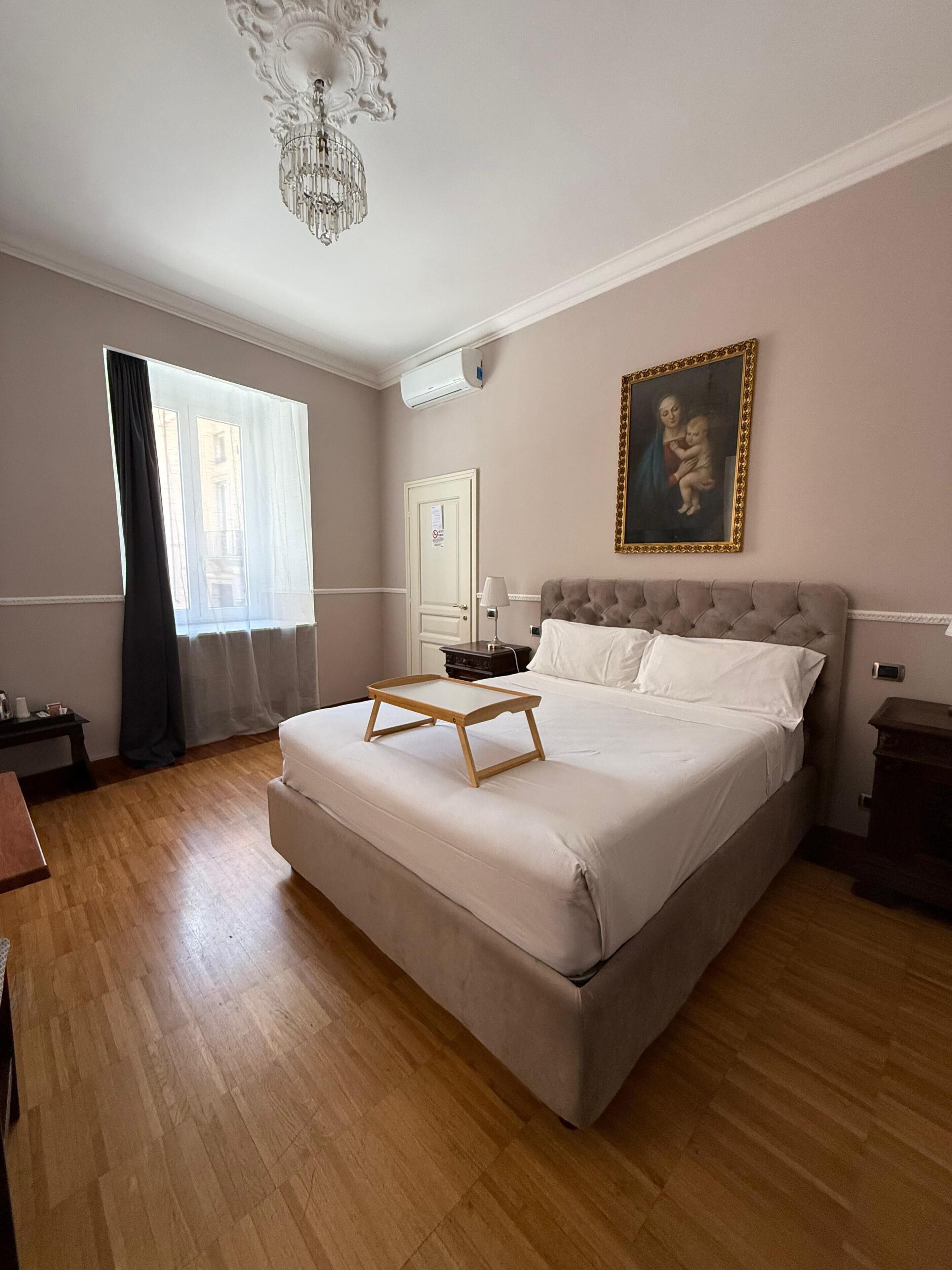 Una camera da letto con un letto grande, un lampadario, un quadro appeso e una finestra con tende.