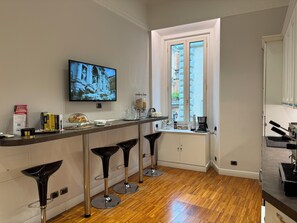 A modern kitchen with a wooden countertop, a TV mounted above it, and a window with a view of buildings. -  I TRE MOSCHETTIERI - D' ARTAGNAN Luxury Guest House (Rome)