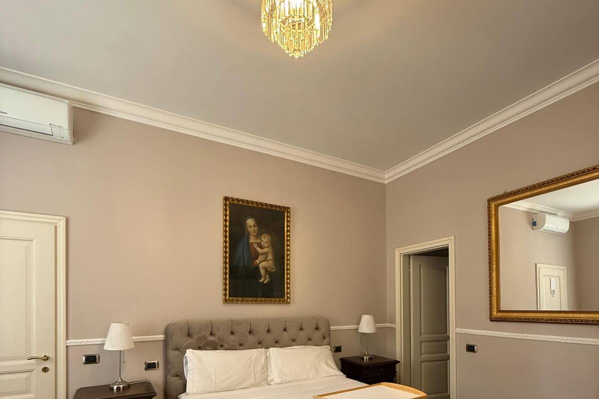 A bedroom with a large bed, a chandelier, a painting, and a mirror.