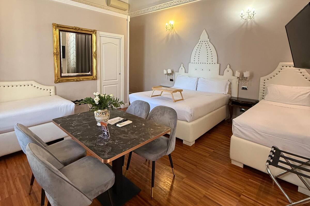 A modern, well-lit room with a wooden ceiling, a dining table with chairs, a sofa, a bed, and a decorative wall piece.