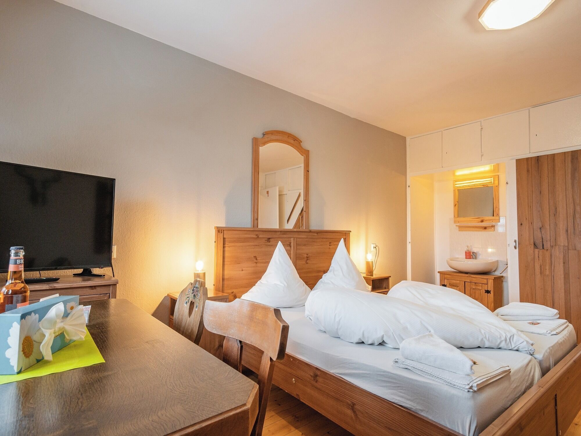 Une chambre à coucher avec un lit en bois, une table de chevet avec une lampe, une télévision et un miroir au-dessus du lit.