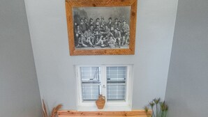 Un escalier en bois avec une rampe blanche, une petite fenêtre à cadre blanc et, au-dessus de la fenêtre, une photographie en noir et blanc encadrée.