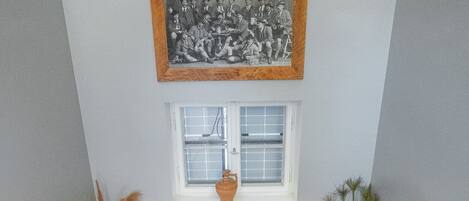 A wooden staircase with a white handrail, a small window with a white frame, and a framed black and white photograph above the window.