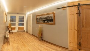 Un couloir doté d’un plancher en bois, d’une porte coulissante de style rustique, d’un tableau représentant un paysage encadré et d’une porte portant l’inscription « Salle 1-9 ».