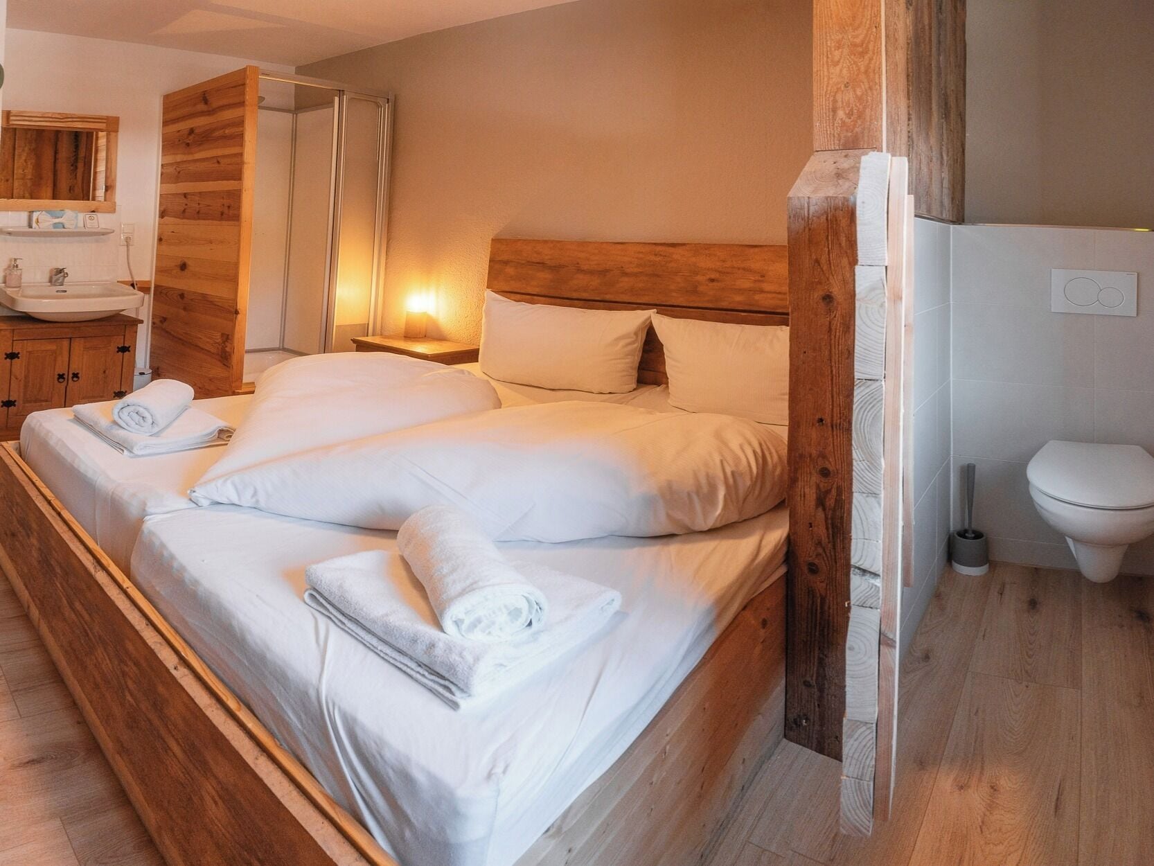 A bedroom with a wooden headboard, a wooden wardrobe, a bedside table with a lamp, and a bathroom with a toilet and sink.
