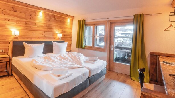 Une chambre avec un grand lit, des boiseries, une fenêtre avec des rideaux et une commode en bois.