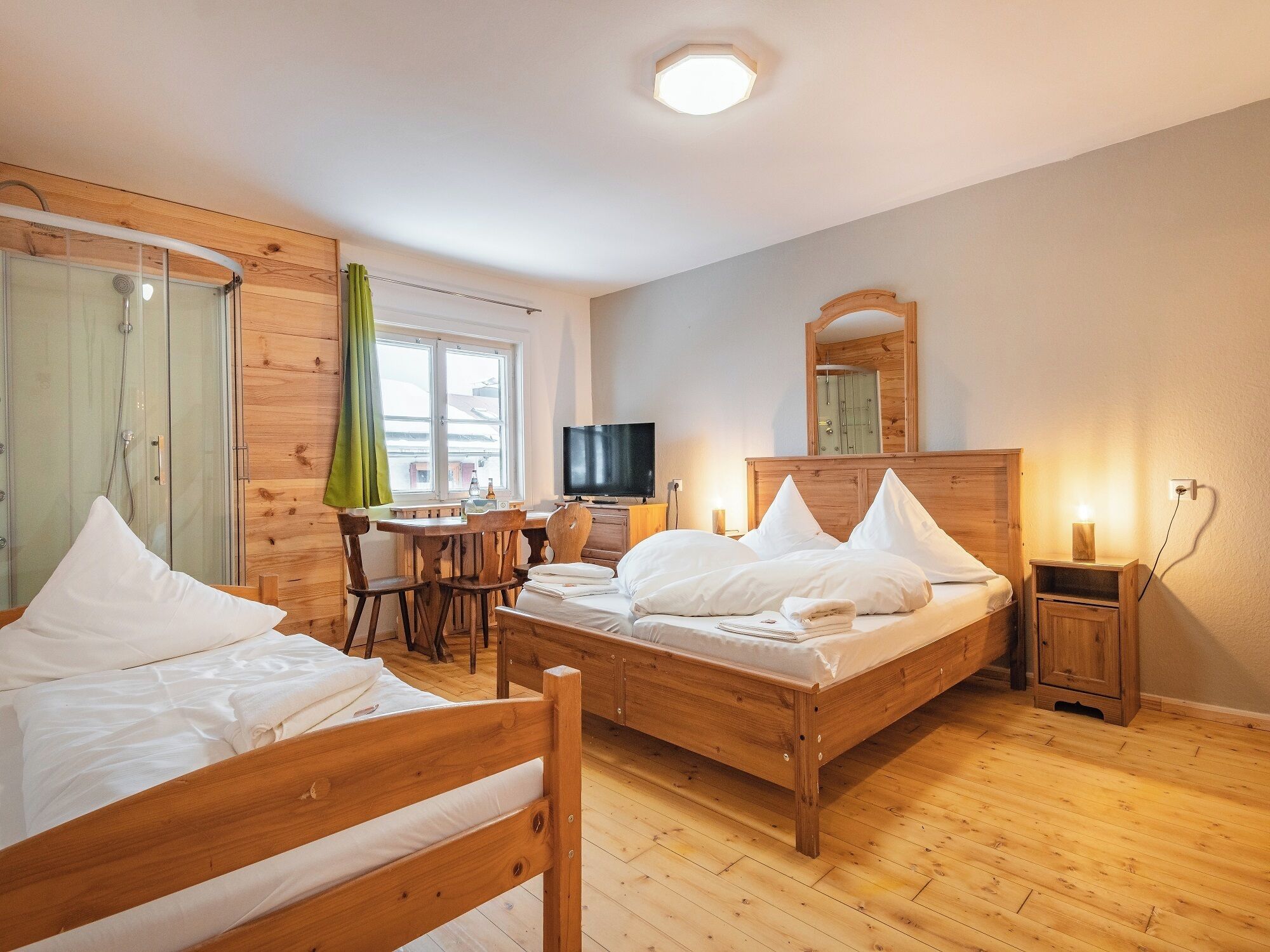 A bedroom with two wooden beds, a desk with a chair, a television, and a mirror.