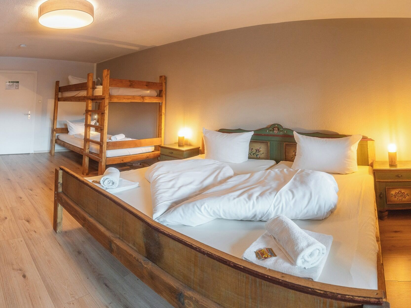 A room with a bunk bed, a single bed, wooden flooring, and a door with a sign.