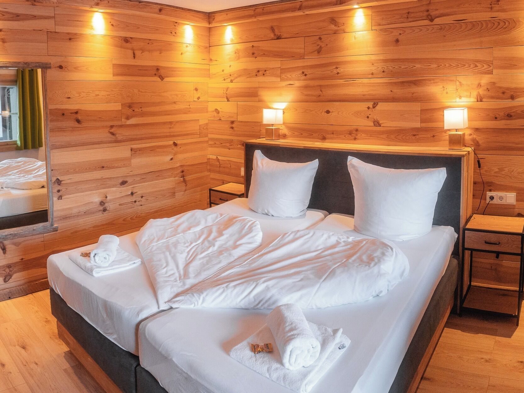 A wooden-paneled room with a bed, two bedside lamps, and a mirror.