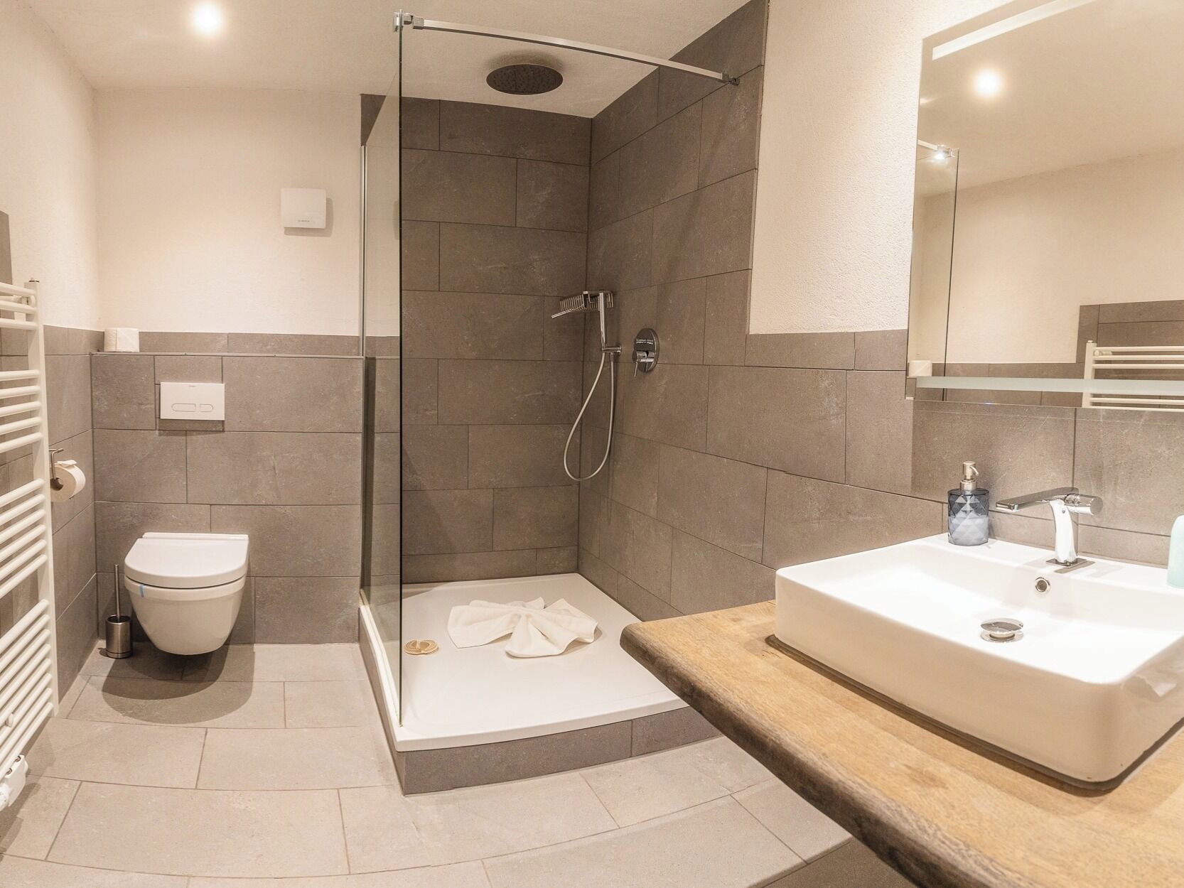 A modern bathroom with a glass-enclosed shower, a white toilet, and a large sink with a wooden countertop.