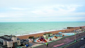 A coastal promenade with a playground, a road, and a building with a flag. - West Beach Hotel (Brighton)