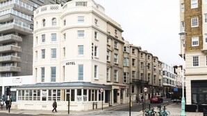 A corner building with a 'HOTEL' sign, featuring a curved facade with multiple windows and balconies. - West Beach Hotel (Brighton)