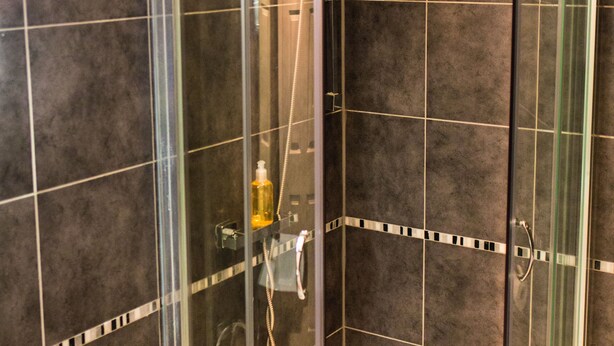 Ducha con paredes de vidrio, bañera blanca y una toalla en el asiento.