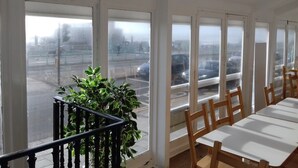 A room with large windows, a staircase, and a dining area with wooden chairs and tables. - West Beach Hotel (Brighton)