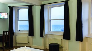 A hotel room with two windows, a bed with white linens, a chair, and a radiator. - West Beach Hotel (Brighton)