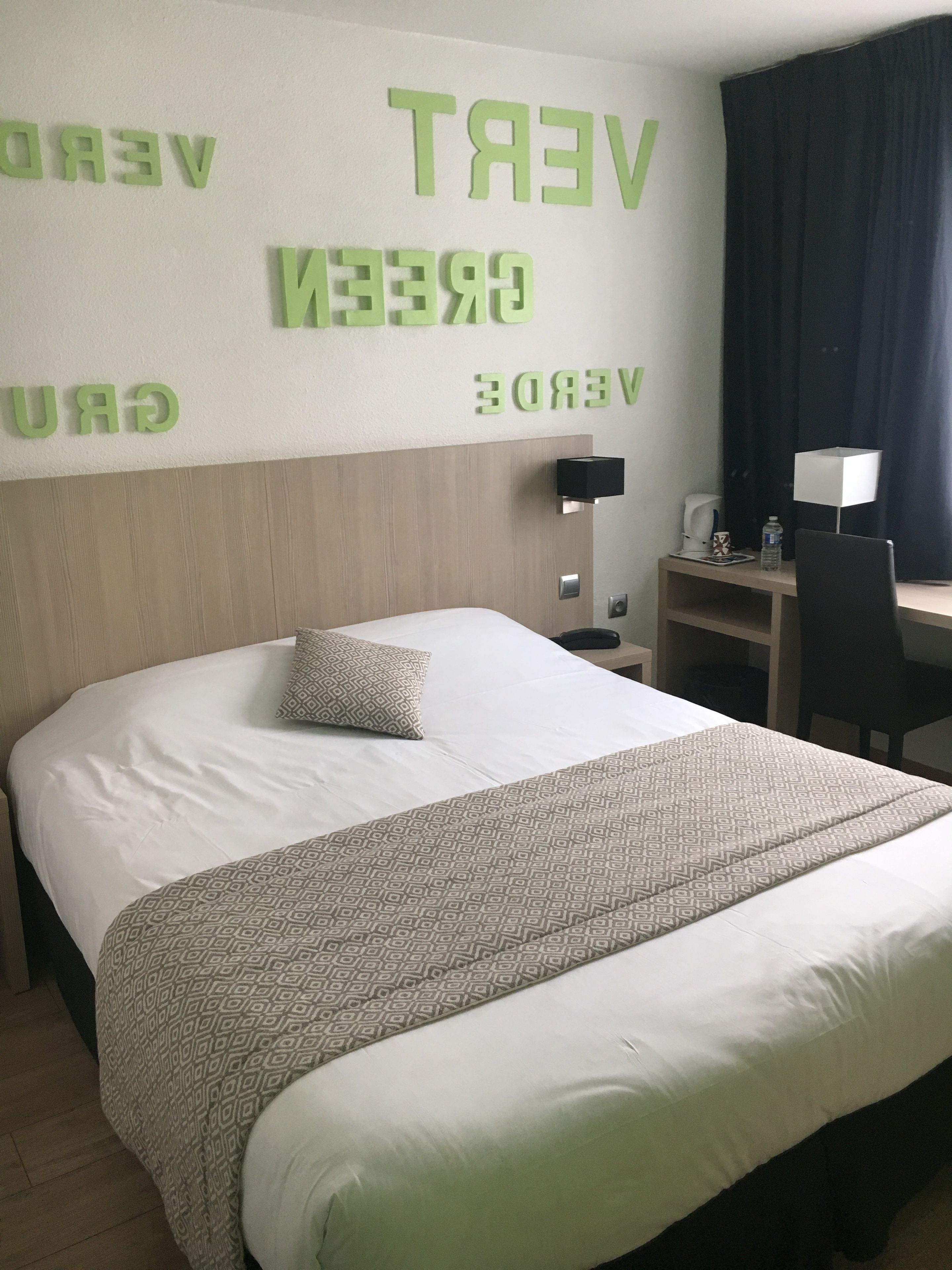 Habitación de hotel con una cama, un escritorio y una pared con letras verdes que deletrean "GREEN VERT".