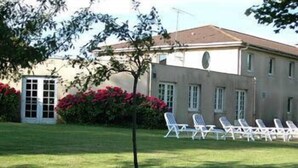 A building with a garden area featuring a row of white lounge chairs and a small tree. - Hôtel Relais d'Etretat (Bolbec)