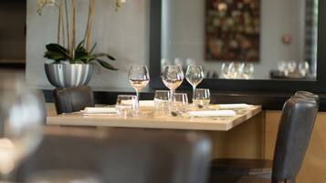 Un coin repas avec une table dressée pour deux personnes, un pot d’orchidée et un menu encadré accroché au mur.