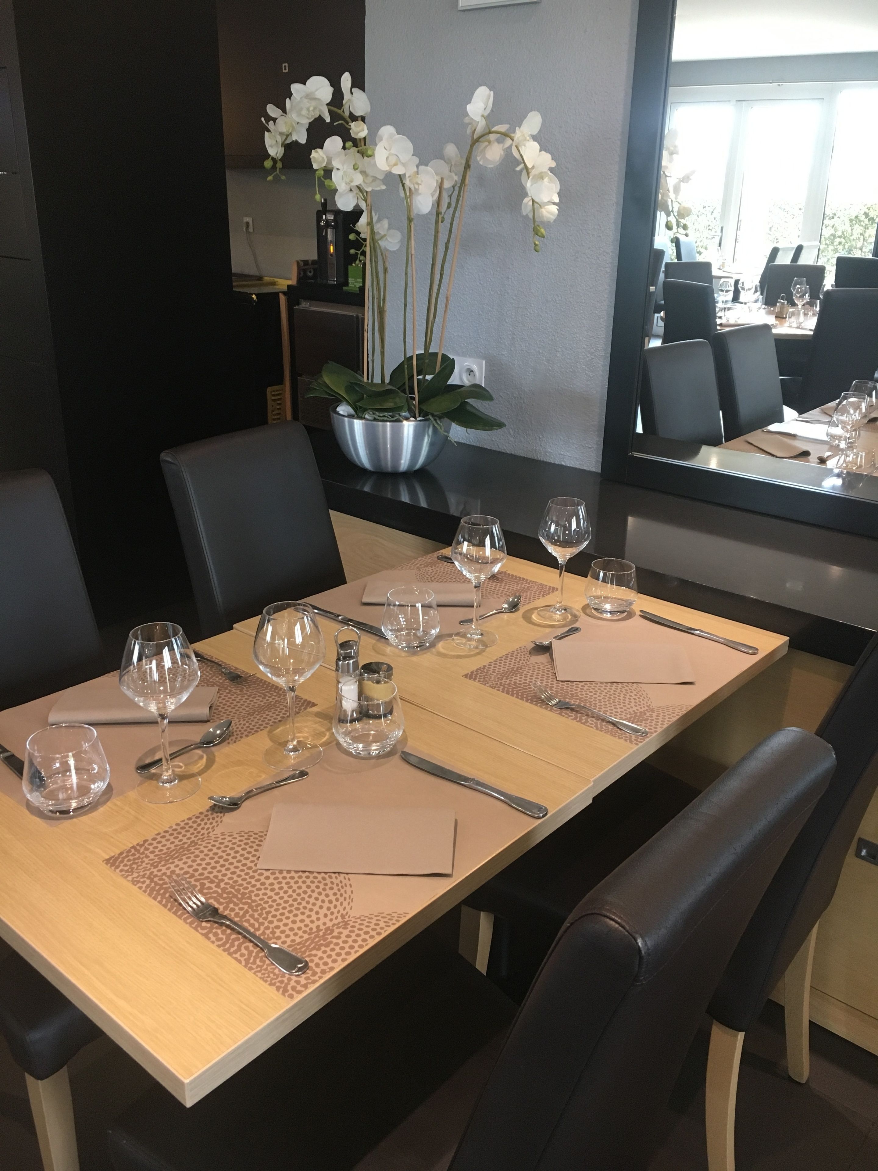 A dining table set with wine glasses, cutlery, and place settings in a modern dining area with black chairs and a large window.