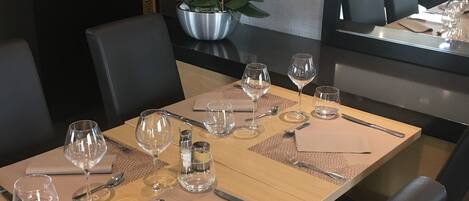 Mesa de comedor dispuesta con copas de vino, cubiertos y vajilla en un espacio moderno con sillas negras y un gran ventanal.