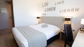 Habitación de hotel con una cama, un escritorio y una silla. Hay luces en la pared y un letrero con el nombre del hotel.