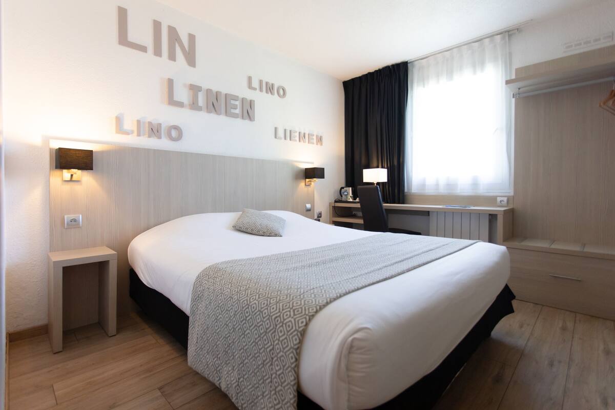 A hotel room with a large bed, bedside tables, a desk, and a window with curtains.