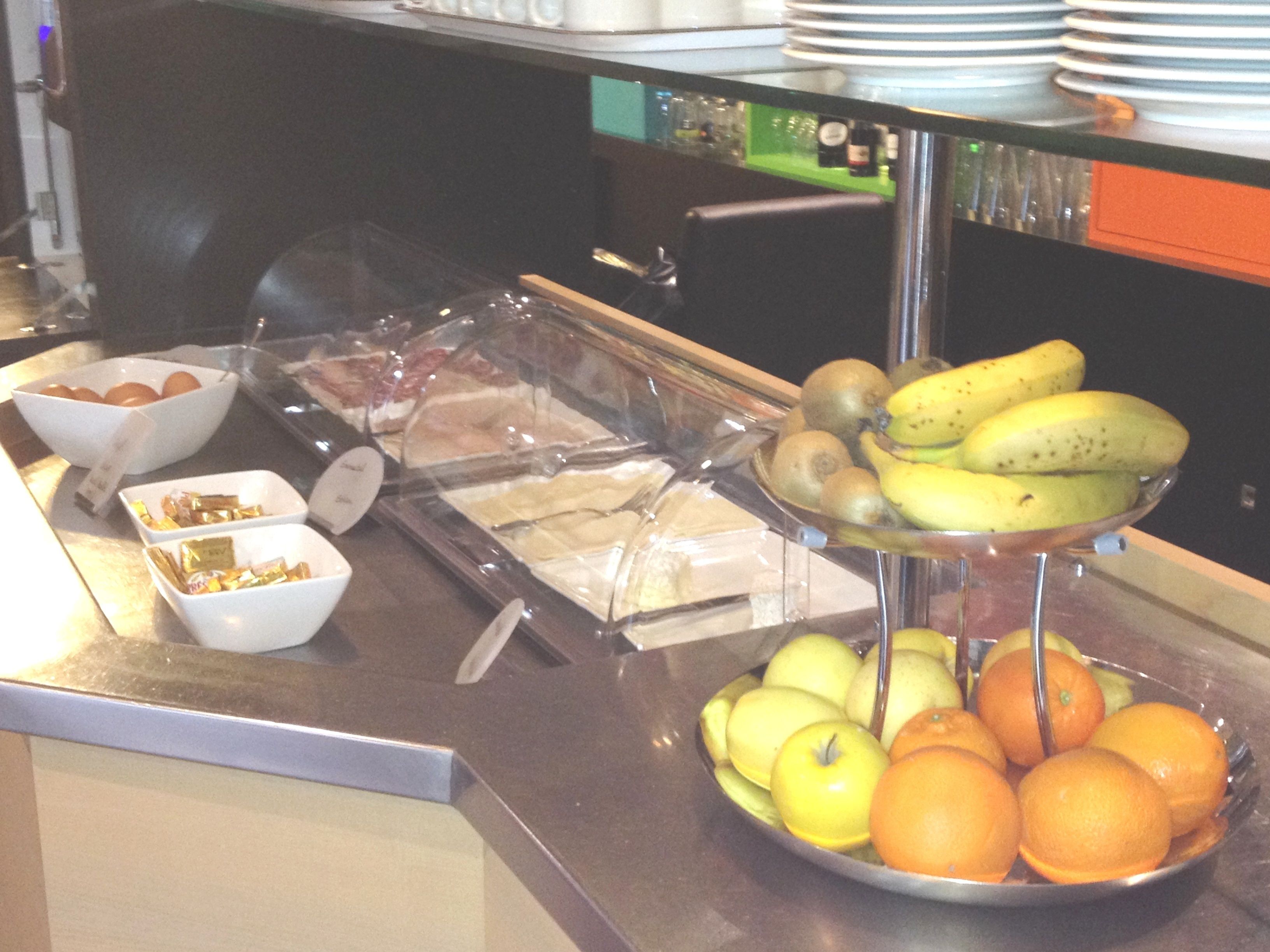 Un buffet con diversi cibi, tra cui uova, pane, banane, mele e arance.