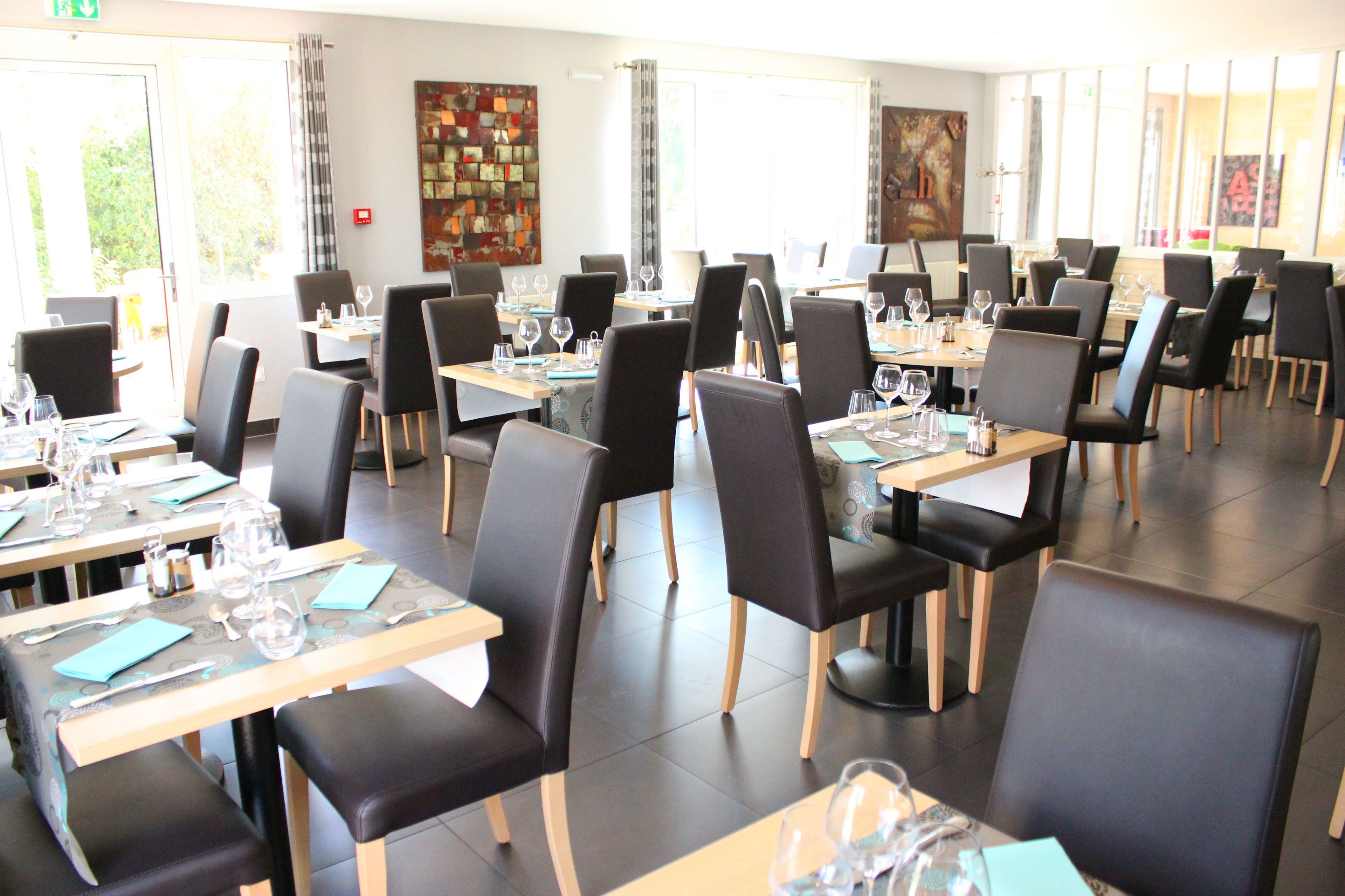 A restaurant with multiple tables and chairs, each set with wine glasses and cutlery.