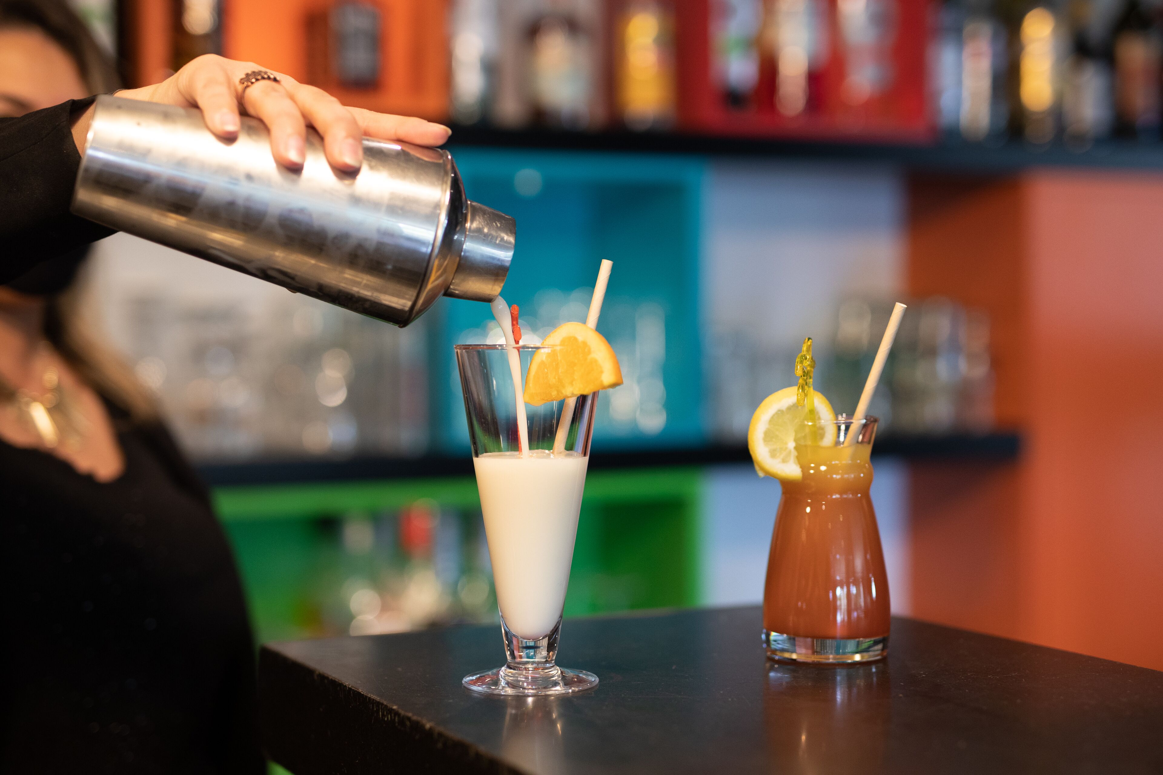 A bartender pouring a drink into a glass with a lemon slice and straw.