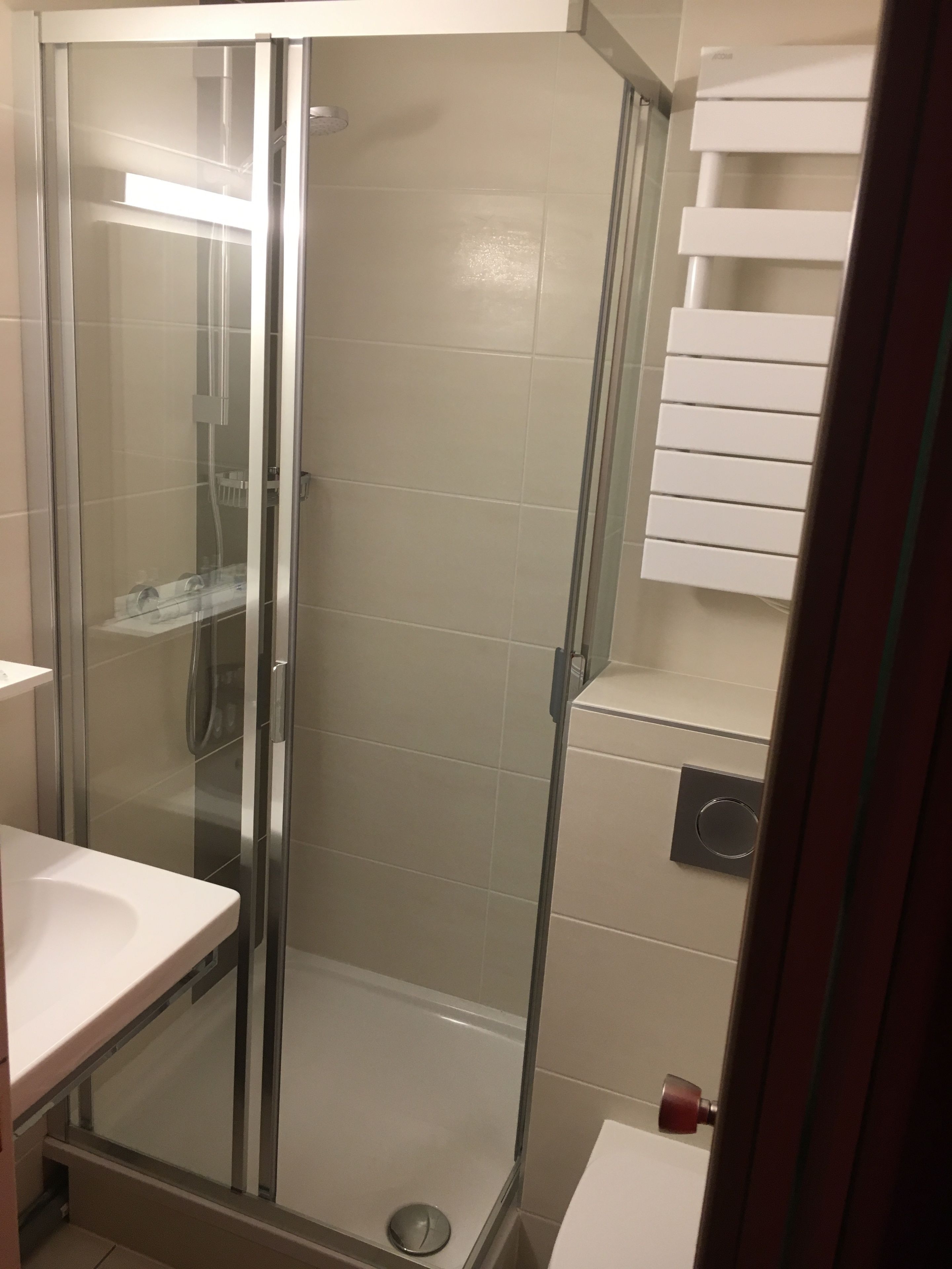 A glass-enclosed shower stall with a white sink and a towel rack to the right.