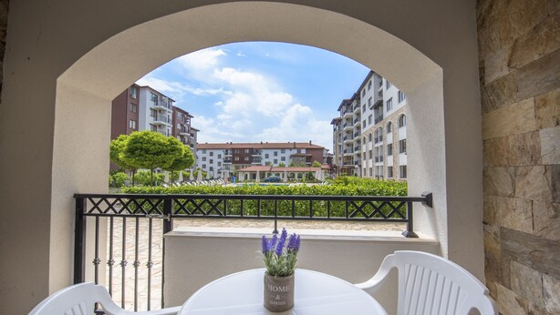 A balcony with a table and chairs, a potted plant, and a view of multi-story buildings. - Apollon Apartments (Nessebar)