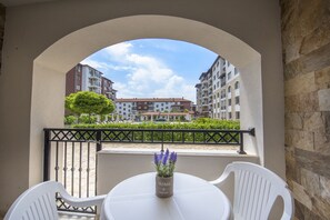 Un balcon avec une table et des chaises, un pot de fleurs et une vue sur des immeubles à plusieurs étages.