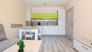 A compact kitchen with white and green cabinets, a microwave, and a sink. There's a dining table with chairs and a small plant on the table. - Apollon Apartments (Nessebar)