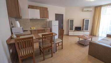 A modern kitchen with wooden cabinets, a dining area with a table and chairs, a small refrigerator, and a television in a cabinet.