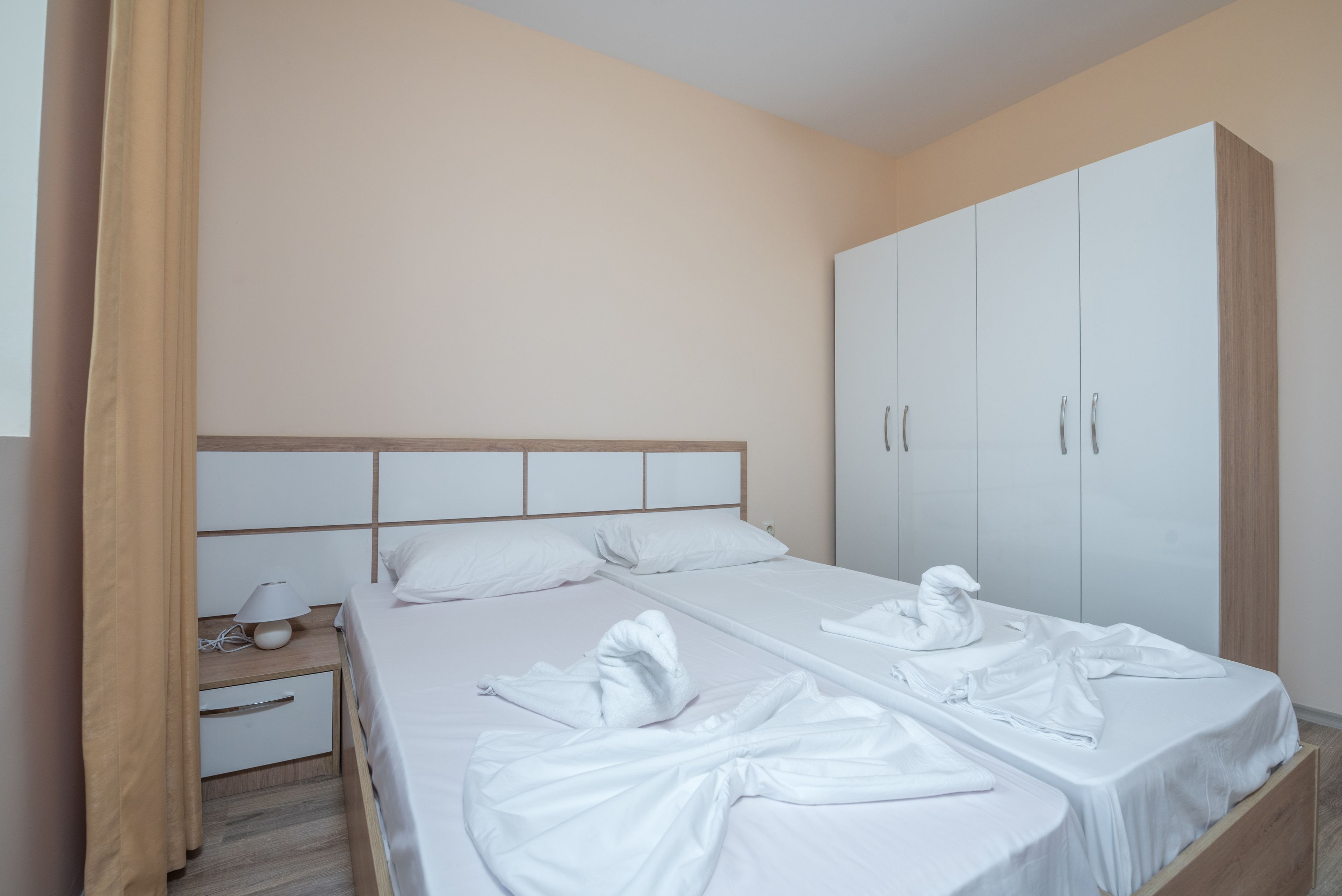 Ein Hotelzimmer mit zwei Betten, einem Schrank, einem Nachttisch mit Lampe und einem Vorhang.