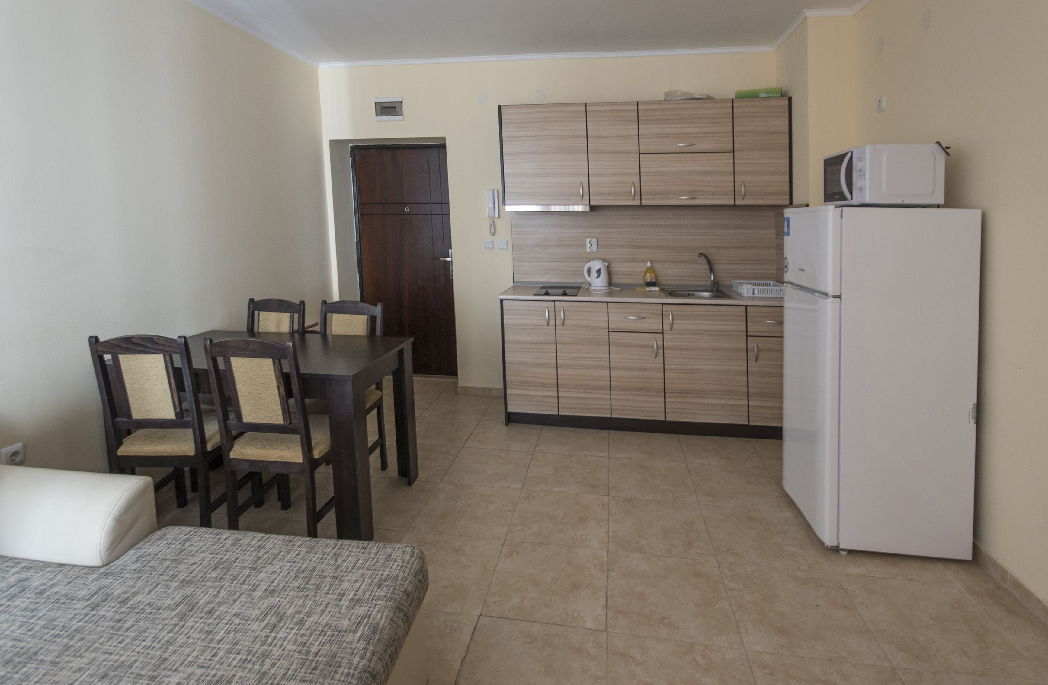 A compact kitchen with wooden cabinets, a microwave, a refrigerator, and a dining area with a table and chairs.